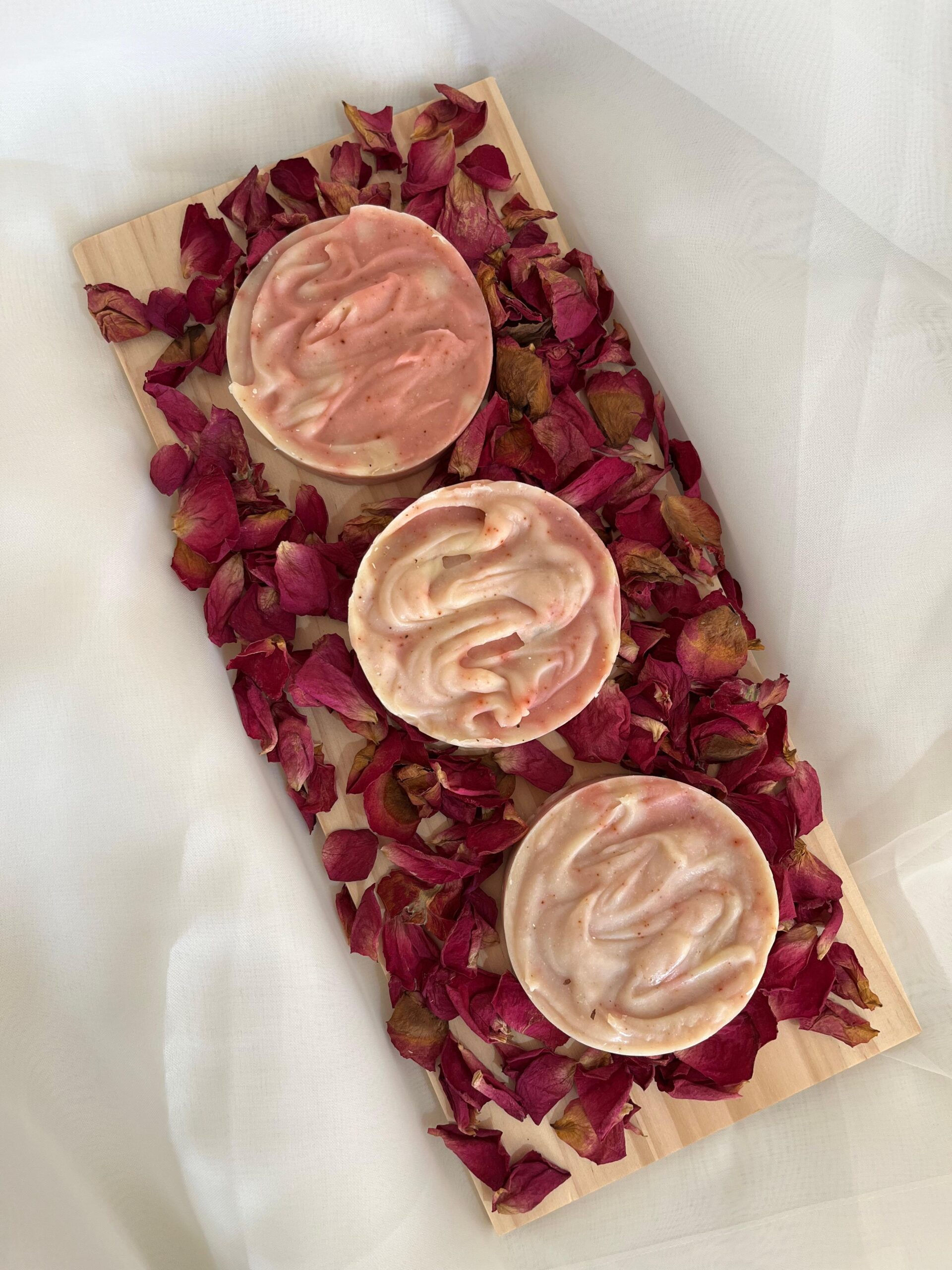 שלושה סבוני פנים ורודים עם עלי כותרת ורדים מסביב